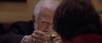 Movie still from “Mrs. Doubtfire” (1993), directed by Chris Columbus – An older man holding a glass of wine and smiling; Extreme Close Up shot, Over the shoulder angle