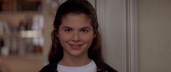 Movie still from “Mrs. Doubtfire” (1993), directed by Chris Columbus – A young girl smiles for the camera in front of a wall; Close Up shot, High angle