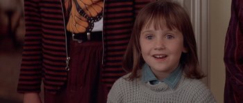 Movie still from “Mrs. Doubtfire” (1993), directed by Chris Columbus – A little girl in a sweater smiles for the camera; Close Up shot, Over the shoulder angle