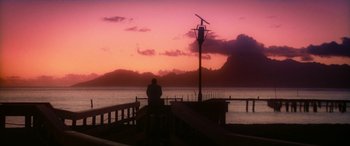 A man sitting on a pier watching the sun go down over the ocean