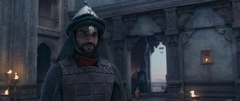 Movie still from “Padmaavat” (2018), directed by Sanjay Leela Bhansali – A man wearing a helmet and armor standing in front of an archway; Medium shot, Over the shoulder angle