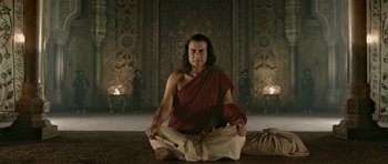 Movie still from “Padmaavat” (2018), directed by Sanjay Leela Bhansali – A man sitting on the ground wearing a red shirt; Medium shot, Low angle