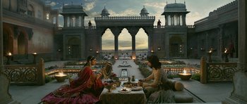 Movie still from “Padmaavat” (2018), directed by Sanjay Leela Bhansali – Two people sitting at a table with food on it in front of a building; Extreme Wide shot, Low angle