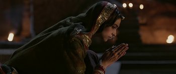 Movie still from “Padmaavat” (2018), directed by Sanjay Leela Bhansali – A woman in a green and gold dress praying; Medium shot, High angle