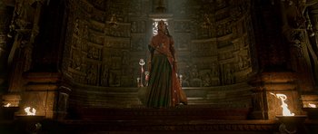 Movie still from “Padmaavat” (2018), directed by Sanjay Leela Bhansali – A woman dressed in traditional indian garb stands in front of a wall with many statues; Wide shot, Low angle