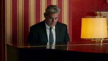 Movie still from “Pain and Glory” (2019), directed by Pedro Almodóvar – A man in a suit and tie playing a piano in front of a red striped wall; Medium shot, Low angle