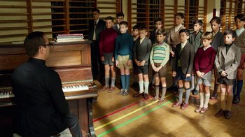 Movie still from “Pain and Glory” (2019), directed by Pedro Almodóvar – A group of young men standing in front of a piano; Wide shot, High angle