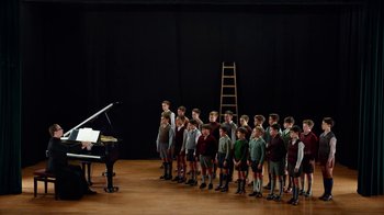 Movie still from “Pain and Glory” (2019), directed by Pedro Almodóvar – A group of young boys standing next to each other in front of a piano; Wide shot, High angle