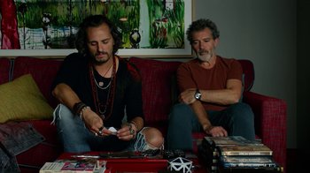 Movie still from “Pain and Glory” (2019), directed by Pedro Almodóvar – A couple of men sitting on top of a red couch; Medium shot, Low angle