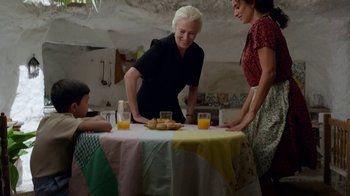 Movie still from “Pain and Glory” (2019), directed by Pedro Almodóvar – Three women and a child standing at a table with food on it; Medium shot, Over the shoulder angle