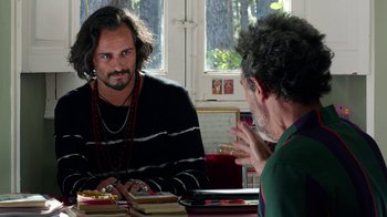 Movie still from “Pain and Glory” (2019), directed by Pedro Almodóvar – Two men sitting at a table talking to each other; Medium shot, Over the shoulder angle