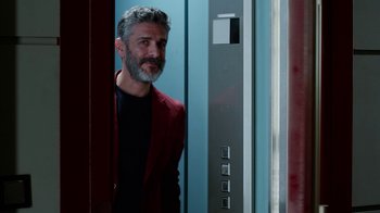 Movie still from “Pain and Glory” (2019), directed by Pedro Almodóvar – A man in a red jacket standing next to an elevator; Medium shot, Over the shoulder angle