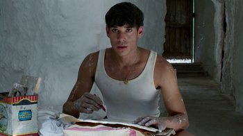 Movie still from “Pain and Glory” (2019), directed by Pedro Almodóvar – A man in a white tank top is writing on a piece of paper; Medium shot, Low angle
