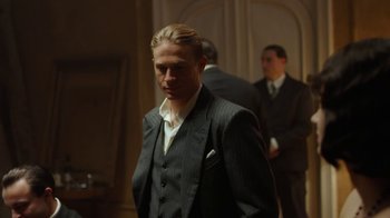 Movie still from “Papillon” (2017), directed by Michael Noer – A man wearing a suit and tie standing in a room; Medium shot, Low angle