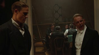 Movie still from “Papillon” (2017), directed by Michael Noer – A group of people sitting around a table; Medium shot, Over the shoulder angle