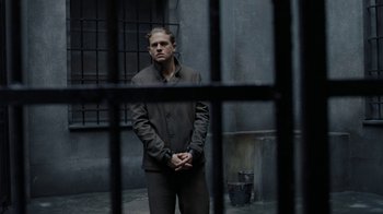 Movie still from “Papillon” (2017), directed by Michael Noer – A man standing in front of a metal cage; Medium shot, Over the shoulder angle
