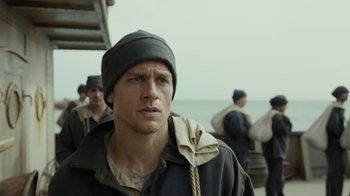 Movie still from “Papillon” (2017), directed by Michael Noer – A person wearing a jacket and a hat; Close Up shot, Over the shoulder angle