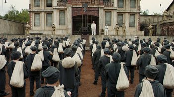 Movie still from “Papillon” (2017), directed by Michael Noer – A large group of men in black suits and white hats; Extreme Wide shot, High angle