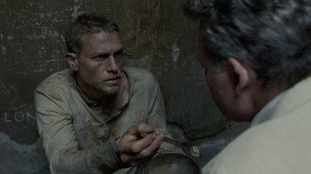 Movie still from “Papillon” (2017), directed by Michael Noer – A man sitting in front of another man in a room; Close Up shot, High angle