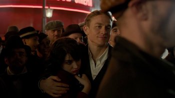 Movie still from “Papillon” (2017), directed by Michael Noer – A man and a woman hugging in a crowd of onlookers; Medium shot, Over the shoulder angle