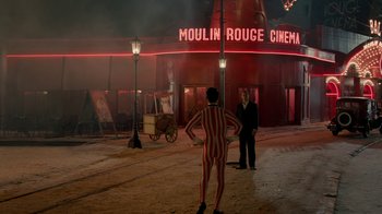 Movie still from “Papillon” (2017), directed by Michael Noer – A man in a red and white striped suit standing in front of a building; Wide shot, Over the shoulder angle