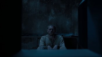 Movie still from “Papillon” (2017), directed by Michael Noer – A man sitting on the ground in a dark room; Medium shot, High angle
