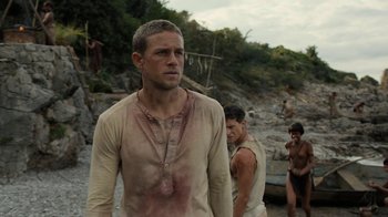 Movie still from “Papillon” (2017), directed by Michael Noer – A group of men standing next to each other on a beach; Medium shot, Over the shoulder angle