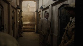 Movie still from “Papillon” (2017), directed by Michael Noer – A man in a suit standing in front of a staircase; Wide shot, Low angle
