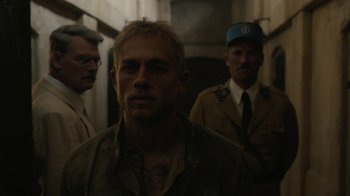 Movie still from “Papillon” (2017), directed by Michael Noer – A man standing next to two other men in a hallway; Close Up shot, Over the shoulder angle