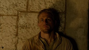 Movie still from “Papillon” (2017), directed by Michael Noer – A person wearing a jacket near a brick wall; Close Up shot, High angle