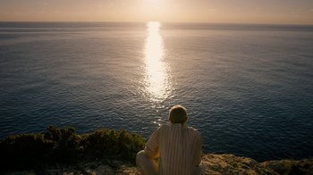 Movie still from “Papillon” (2017), directed by Michael Noer – A man sitting on a cliff looking out at the ocean; Wide shot, High angle