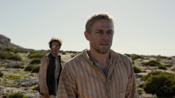 Movie still from “Papillon” (2017), directed by Michael Noer – Two men standing in the desert looking into the distance; Medium shot, Over the shoulder angle