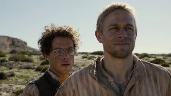 Movie still from “Papillon” (2017), directed by Michael Noer – Two men standing next to each other on a dirt hill; Close Up shot, Over the shoulder angle