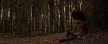 Movie still from “ParaNorman” (2012), directed by Sam Fell – A person sitting on the ground in the woods; Wide shot, High angle