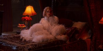 Movie still from “Paradise Hills” (2019), directed by Alice Waddington – A woman sitting on a bed wearing a white dress; Medium shot, High angle