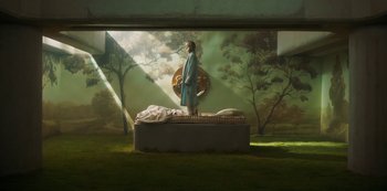 Movie still from “Paradise Hills” (2019), directed by Alice Waddington – A statue of jesus stands on a bed in a room; Wide shot, High angle