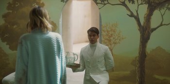 Movie still from “Paradise Hills” (2019), directed by Alice Waddington – A man in a white suit is holding a tray with a pitcher; Medium shot, Over the shoulder angle