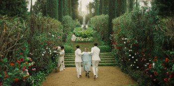 Movie still from “Paradise Hills” (2019), directed by Alice Waddington – A group of people walking down a path in a garden; Wide shot, High angle