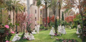 Movie still from “Paradise Hills” (2019), directed by Alice Waddington – A group of people in white dresses sitting in a garden; Extreme Wide shot, High angle