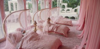 Movie still from “Paradise Hills” (2019), directed by Alice Waddington – A little girl sitting on top of a bed in a pink room; Extreme Wide shot, High angle