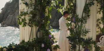 Movie still from “Paradise Hills” (2019), directed by Alice Waddington – A man in a white bathrobe standing next to a garden; Wide shot, High angle