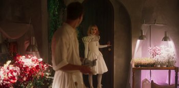 Movie still from “Paradise Hills” (2019), directed by Alice Waddington – A man and a woman dressed in white are standing in front of a door; Wide shot, Over the shoulder angle