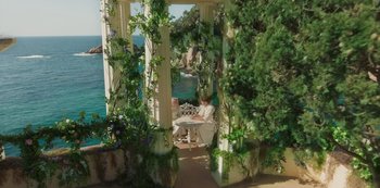 Movie still from “Paradise Hills” (2019), directed by Alice Waddington – Two people sitting at a table on a porch; Extreme Wide shot, High angle