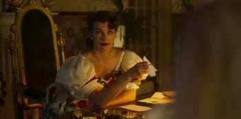Movie still from “Paradise Hills” (2019), directed by Alice Waddington – A woman sitting at a table with a piece of paper in her hand; Medium shot, Over the shoulder angle