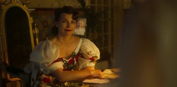 Movie still from “Paradise Hills” (2019), directed by Alice Waddington – A woman sitting at a table in a room; Medium shot, Over the shoulder angle