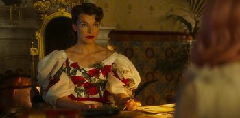 Movie still from “Paradise Hills” (2019), directed by Alice Waddington – A woman sitting at a table holding a knife; Medium shot, Over the shoulder angle