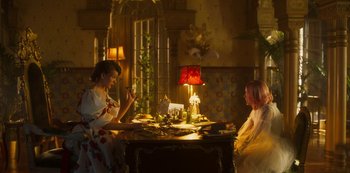 Movie still from “Paradise Hills” (2019), directed by Alice Waddington – Two women sitting at a table in front of a lamp; Wide shot, Low angle