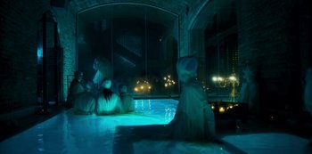 Movie still from “Paradise Hills” (2019), directed by Alice Waddington – A group of people sitting in a room at night; Extreme Wide shot, High angle