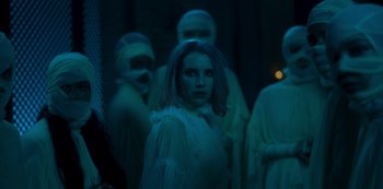 Movie still from “Paradise Hills” (2019), directed by Alice Waddington – A group of people in a dark room; Medium shot, Over the shoulder angle