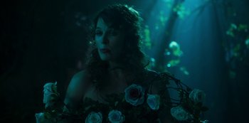 Movie still from “Paradise Hills” (2019), directed by Alice Waddington – A woman with long curly hair standing next to flowers; Close Up shot, Over the shoulder angle